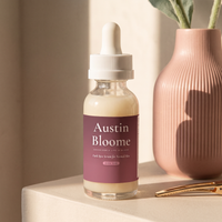 Dark Spot Serum on a plaster ledge in a stripe of afternoon light beside a rose vase
